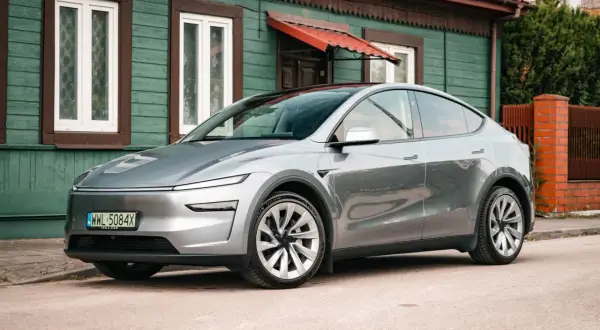 Srebrny Tesla Y stoi przed zielonym domem. Zastanawiasz się, ile koni ma ten model?
