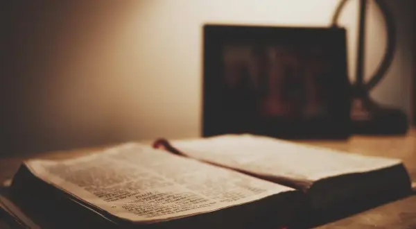 Otwarta Biblia na stole, obok ramka ze zdjęciem. Czy granie w lotto to grzech? Szukamy odpowiedzi w Piśmie Świętym.