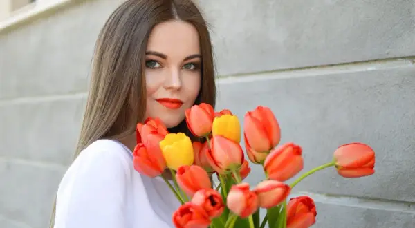 Uśmiechnięta dziewczyna z bukietem pomarańczowych i żółtych tulipanów, idealny prezent na imieniny Anity.