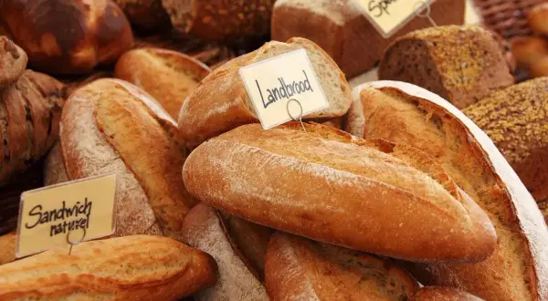 Różnorodne pieczywo, w tym bochenki z etykietami "Landbrood" i "Sandwich naturel". Zastanawiasz się, czym smarować chleb przed pieczeniem, by uzyskać chrupiącą skórkę?