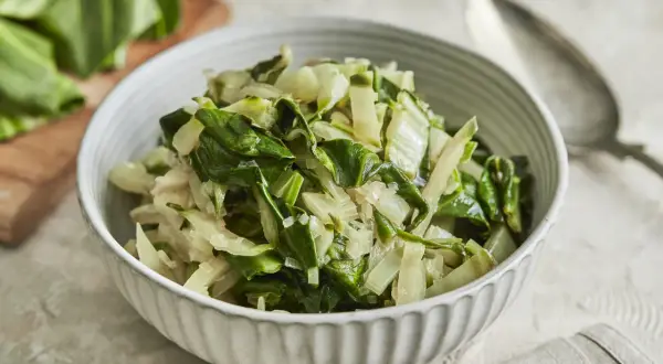 Schüssel mit gedünstetem Mangold, perfekt für ein einfaches Mangold Rezept. Frische Blätter liegen daneben.