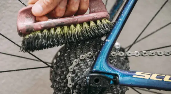 Mit Hausmitteln die Fahrradkette reinigen: Eine Bürste schrubbt die Kette und Kassette des glänzenden blauen Fahrradrahmens.