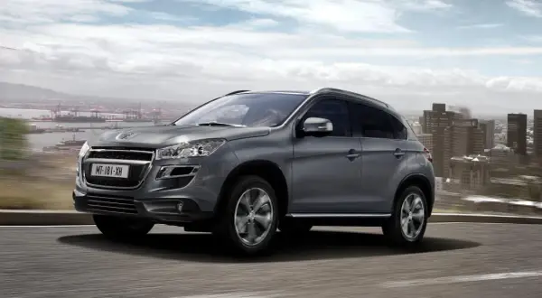 Szary Peugeot 4008 jedzie po drodze z widokiem na miasto i port.