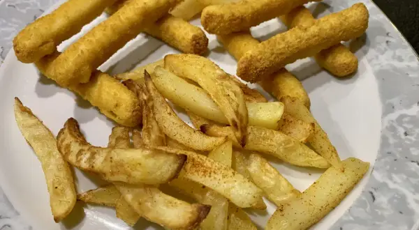 Ein Teller mit knusprigen belgischen Pommes, einige dick geschnitten, andere als Stäbchen frittiert.