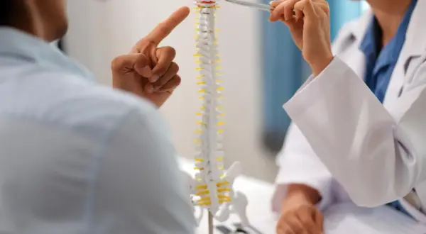 Lekarz pokazuje pacjentowi model kręgosłupa, wskazując na tylną wypuklinę krążka międzykręgowego.