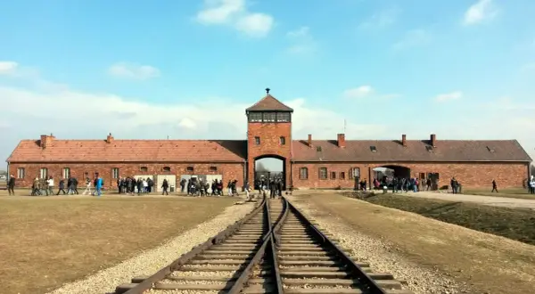 Brama obozowa Auschwitz I z wieżą, tory kolejowe prowadzące do niej. Zwiedzający zastanawiają się, ile trwa zwiedzanie Auschwitz, by poznać historię.