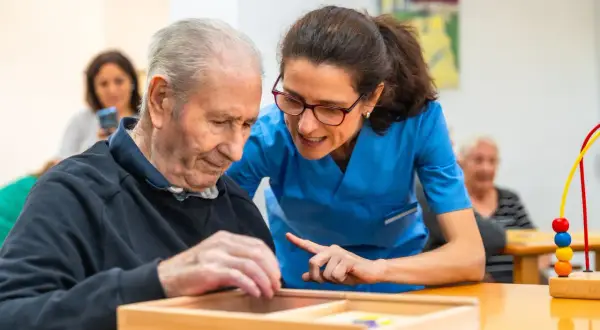 Un homme âgé participe à un atelier sensoriel, guidé par une aide-soignante attentive.