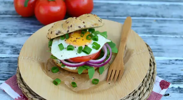 Pyszny burger z jajkiem sadzonym, rukolą, pomidorem i czerwoną cebulą na desce z drewna.