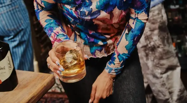 Kobieta trzyma szklankę z whisky Ballantine's. Zastanawia się, ile procent ma ten wyborny trunek.