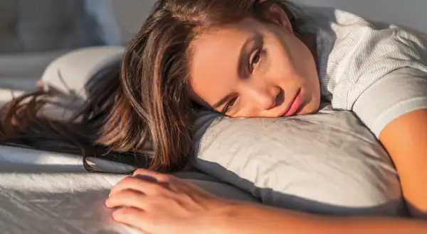 Donna sdraiata sul cuscino, con sguardo stanco e capelli lunghi. Potrebbe soffrire di anemia sideropenica.