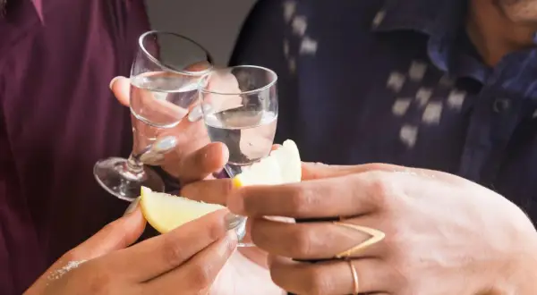 Två personer skålar med små glas med klar alkohol. Citronklyftor och salt ligger redo för att förhöja smaken av gaba alkohol.
