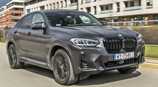 Eleganckie BMW X4 w kolorze grafitowym pędzi ulicą, za kierownicą siedzi mężczyzna.