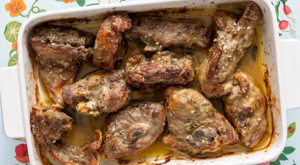 Pezzi succulenti di abbacchio alla romana cotti in teglia, dorati e profumati, pronti per essere gustati.