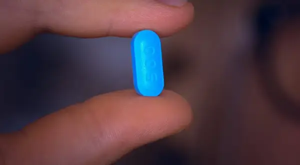 En blå tablett med siffran 500 hålls mellan fingrarna, en påminnelse om att motverka diarré vid penicillin.