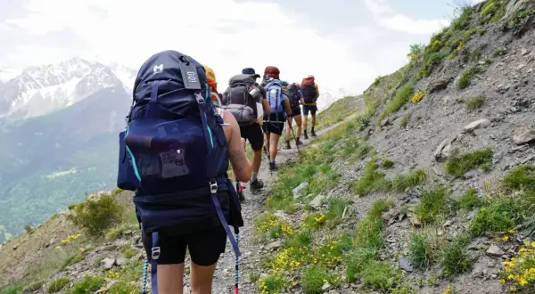 Groupe de randonneurs avec de gros sacs à dos sur un sentier de montagne. Le mot "GO!" est visible sur un sac.
