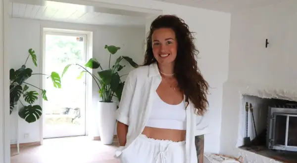 Nathalie Steffner ler mot kameran i ett ljust rum med stora gröna växter och en öppen spis.