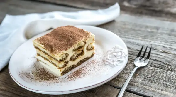 Une part de tiramisu maison, saupoudrée de cacao, sur une assiette blanche, prête à être dégustée. La conservation de ce délice est essentielle.