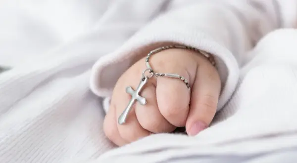Dziecięca dłoń z krzyżykiem na bransoletce, symbol błogosławieństwa. Planujesz jak zorganizować chrzciny?