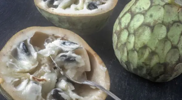 Dwa przekrojone owoce cherimoya, jeden z widelcem, ukazują kremowy miąższ i czarne pestki. Ich słodki, tropikalny smak kusi.