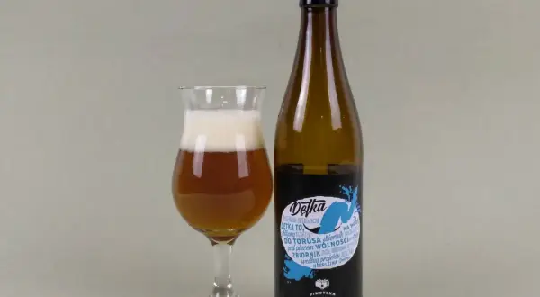 Szklanka z bursztynowym piwem i pianką obok butelki piwa typu new england ipa. Etykieta "Detka" z niebieskim motywem wodnym.