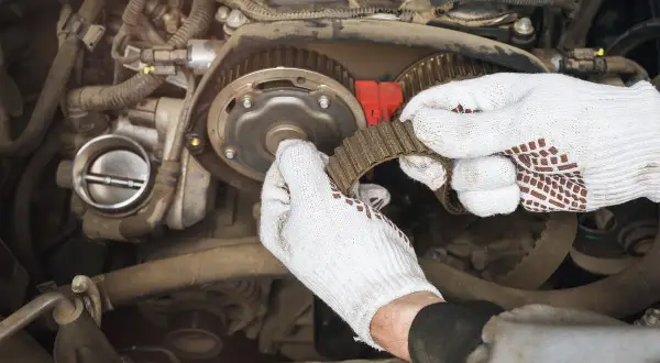 Mechanik w białych rękawiczkach wymienia pasek rozrządu. Czas pracy: ile trwa wymiana rozrządu?