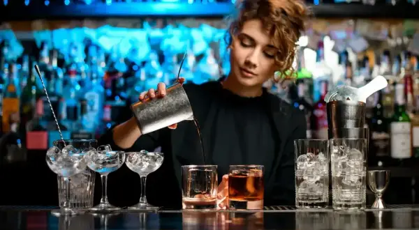 Młody barman przygotowuje drinka, przelewając płyn z shakera do szklanki.