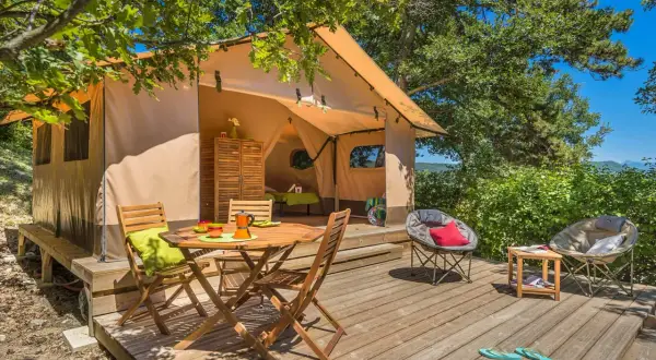 Tente aménagée pour un séjour insolite dans la Drôme, avec terrasse en bois, mobilier de jardin et vue sur la nature.