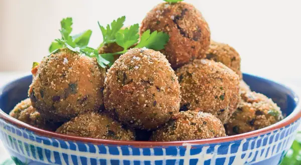 Polpette di melanzane siciliane dorate e croccanti, guarnite con prezzemolo fresco, in una ciotola blu decorata.