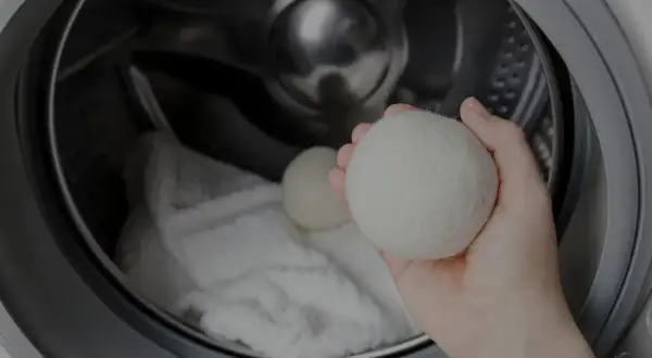 Mano che tiene una pallina per lavatrice, pronta per essere inserita nel cestello con il bucato. Scopri come si usa per un bucato più morbido.