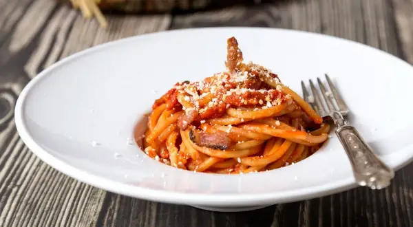Un piatto di bucatini all'amatriciana, con guanciale croccante e una salsa rossa, spolverata di pecorino. La ricetta originale amatriciana cipolla, un classico intramontabile.