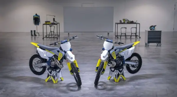 Dwa motocykle crossowe Husqvarna TC 125 w białym i żółtym kolorze stoją na stojakach.