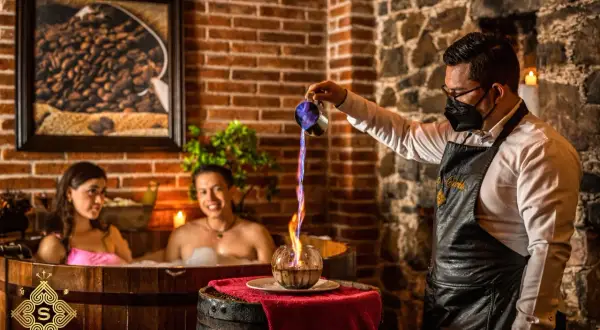 Pareja disfruta de un baño de chocolate spa mientras un mesero vierte líquido en llamas.