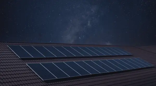 Paneles solares en un tejado bajo un cielo estrellado. La imagen sugiere que los paneles solares funcionan de noche, capturando la energía de las estrellas.