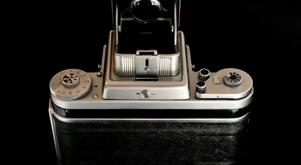 A vintage Pentacon Six camera, with its viewfinder open, sits on a reflective black surface.