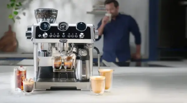 Macchina per caffè De'Longhi in azione, con chicchi pronti per la produzione del caffè. Un uomo assapora una bevanda calda.