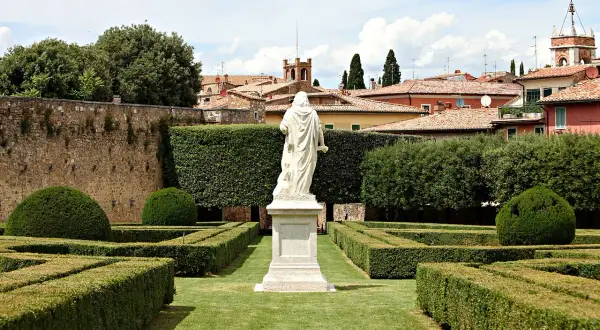 Statua bianca al centro degli Horti Leonini, con siepi geometriche e un muro di pietra.
