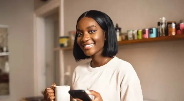 Lächelnde Frau mit Kaffee und Handy. Perfekt für die Darstellung von Teilzeit-Arbeit und dem Zeitaufwand, den sie mit sich bringt.
