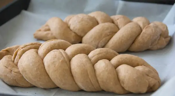 Dwie plecione chałki na papierze do pieczenia. Zastanawiasz się nad chałka kcal?