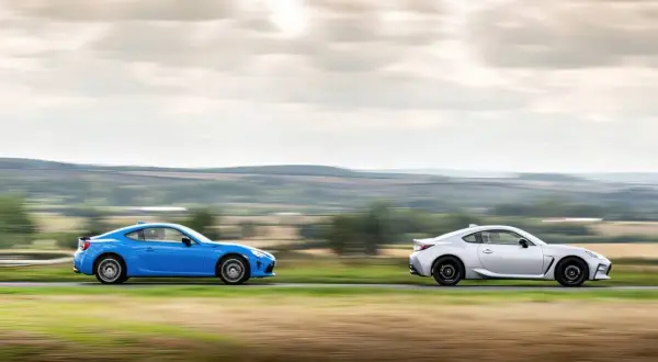 Dwa sportowe samochody, niebieska i srebrna Toyota 86, pędzą po wiejskiej drodze, tworząc dynamiczny obraz.