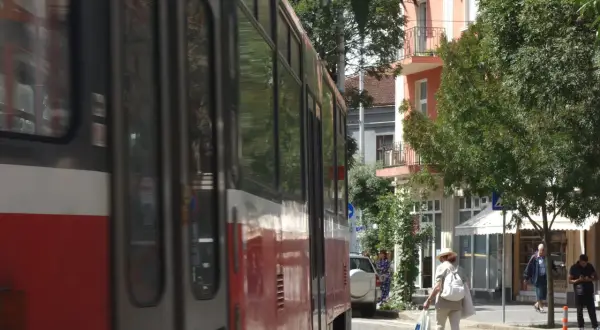 Przejeżdżający tramwaj w słoneczny dzień w Sofii. Kobieta w kapeluszu idzie ulicą z torbami.