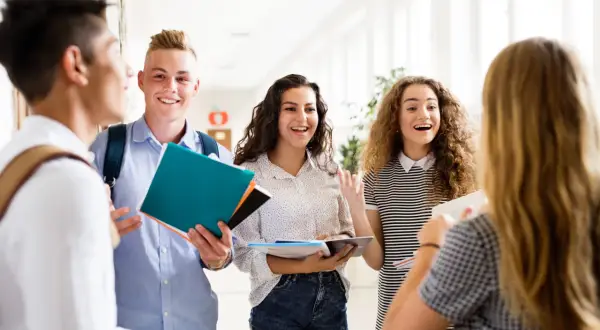 Uczniowie rozmawiają na korytarzu, trzymając książki. Czy na studium trzeba mieć maturę? To pytanie nurtuje wielu młodych ludzi.
