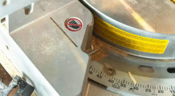 Detalle de una sierra ingletadora con marcas de ángulo para saber como medir para cortar a inglete. Se ve una advertencia de seguridad.