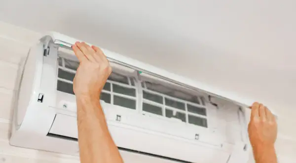 Mains ouvertes pour le nettoyage clim. Les filtres sont visibles à l'intérieur de l'unité murale.
