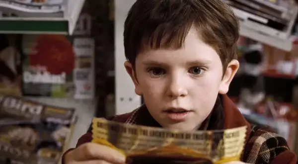 Chłopiec z filmu "Charlie i fabryka czekolady" trzyma złoty bilet. Freddie Highmore w tej roli to początek jego kariery w filmach, serialach i programach.