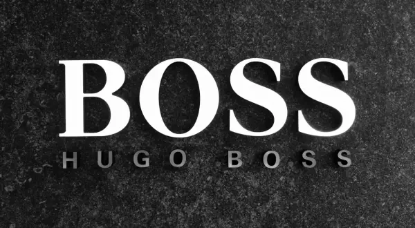 Białe litery "BOSS" na ciemnym, kamiennym tle. Poniżej mniejsze litery "HUGO BOSS". To symbol marki z bogatą historią.