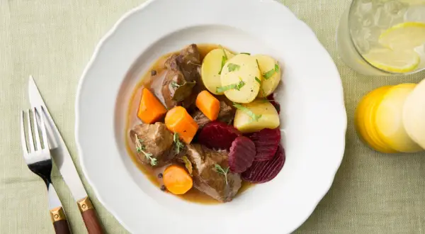 En tallrik med skånsk kalops, kött, morötter, potatis och rödbetor. Serveras med en drink med citron och is.