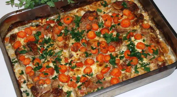 Pyszna szynka pieczona w plastrach z marchewką i natką pietruszki, gotowa na obiad.