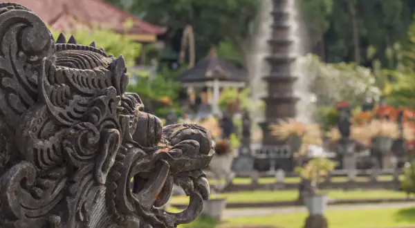 Eine detaillierte Steinskulptur eines Fabelwesens im Vordergrund, im Hintergrund ein Garten mit Brunnen und Pflanzen.