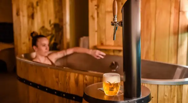 Entspannende Frau in einem Bierfass-Bad, daneben ein frisch gezapftes Pils. Ein einzigartiges Bier-Spa-Erlebnis in Pilsen.