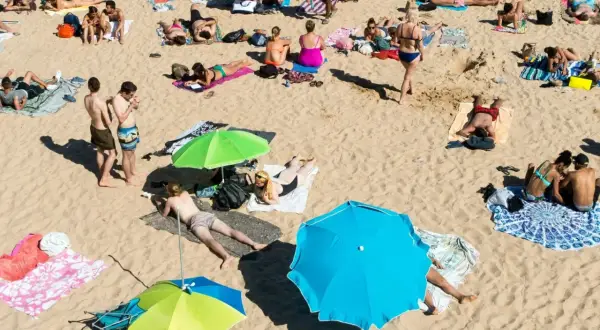 Wakacje pod gruszą na plaży. Ludzie opalają się, odpoczywają pod parasolami, ciesząc się słońcem i piaskiem.